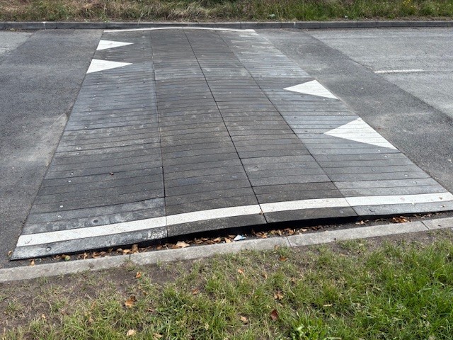 Sinusoidal rubber ramp installed across a full-width roadway, providing smooth traffic calming with directional road markings.