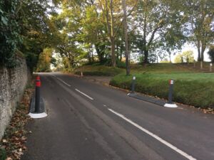 Pair of satellite traffic islands installed on a rural road, formed with modular kerbing and fitted with bollards to narrow the carriageway and manage vehicle speeds.