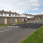 Combination raised table installed on a road, featuring Traficop rubber ramp modules with white directional arrow markings and an infilled central section for traffic calming.