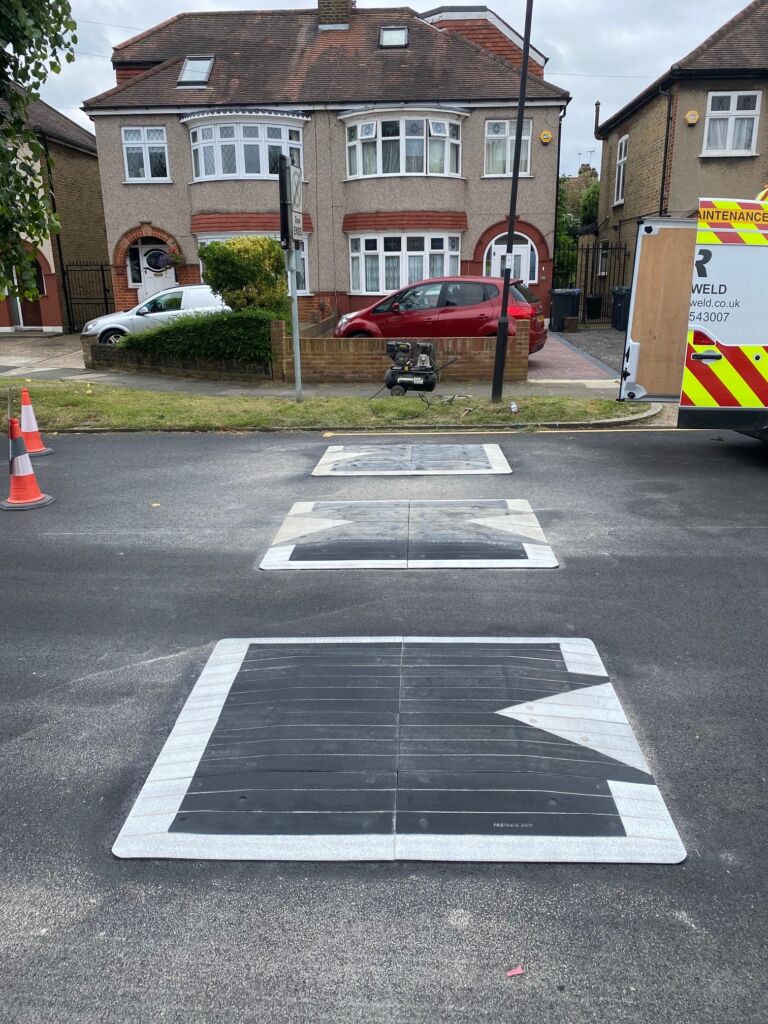 Traficop rubber speed cushions installed on a residential road, featuring white perimeter markings and large directional arrows for traffic guidance