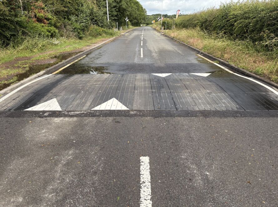 Sinusoidal rubber ramp installed across a full-width roadway, providing smooth traffic calming with directional road markings.