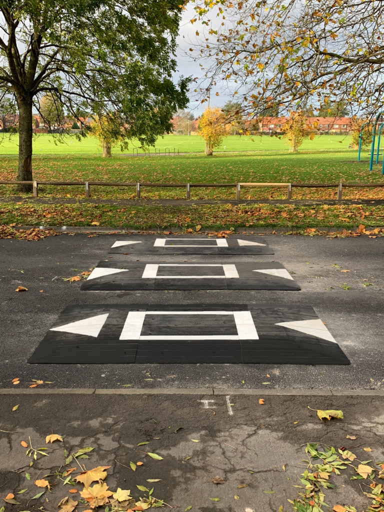 Traficop rubber speed cushions installed on a roadway, featuring white markings and directional arrows for traffic calming.