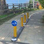 Milestone islands with reflective pole cones installed along a shared pedestrian and cycle path, providing physical separation and guidance at a curve in the route.