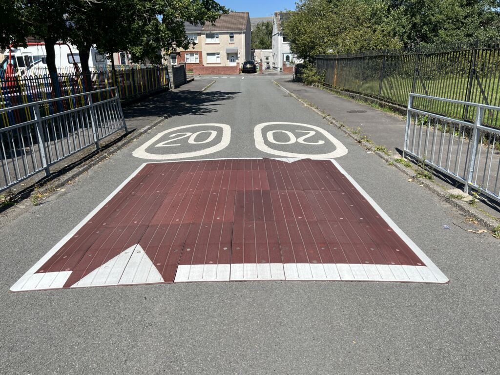 Raised rubber speed table installed on a residential road, with contrasting surface and road markings to slow vehicle traffic near a pedestrian area.