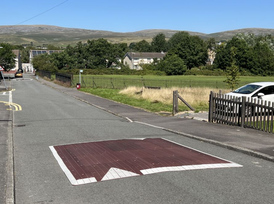 Raised rubber speed table installed on a residential road, with contrasting surface and road markings to slow vehicle traffic near a pedestrian area.