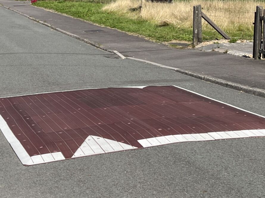 Raised rubber speed table installed on a residential road, with contrasting surface and road markings to slow vehicle traffic near a pedestrian area.