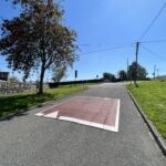Raised rubber speed table installed on a residential road, with contrasting surface and road markings to slow vehicle traffic near a pedestrian area.