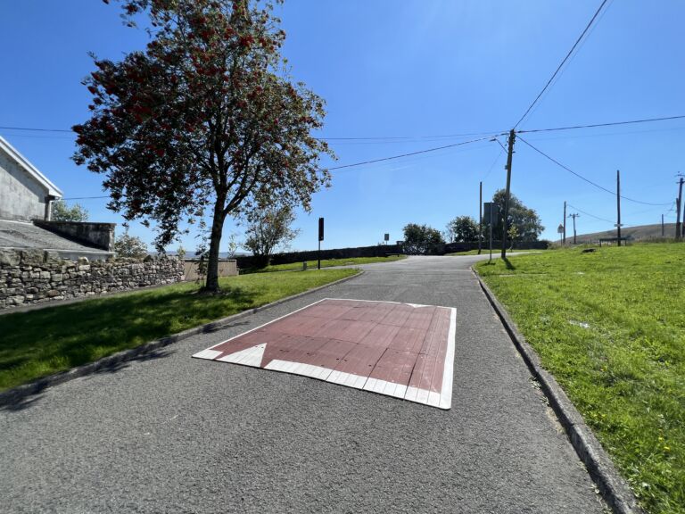 Raised rubber speed table installed on a residential road, with contrasting surface and road markings to slow vehicle traffic near a pedestrian area.