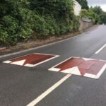 Two Traficop rubber speed cushions installed on a road, featuring red surface panels with white perimeter markings and directional arrows.