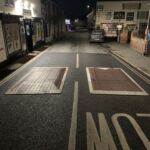 Two Traficop rubber speed cushions installed on a road at night, each outlined with white edge markings and directional arrows for visibility and traffic calming.