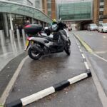 Half Battered (HB) RediKerb kerbing forming a raised island at a shopping centre entrance, separating a footway from a bus stop area with a motorcycle parked on the island.