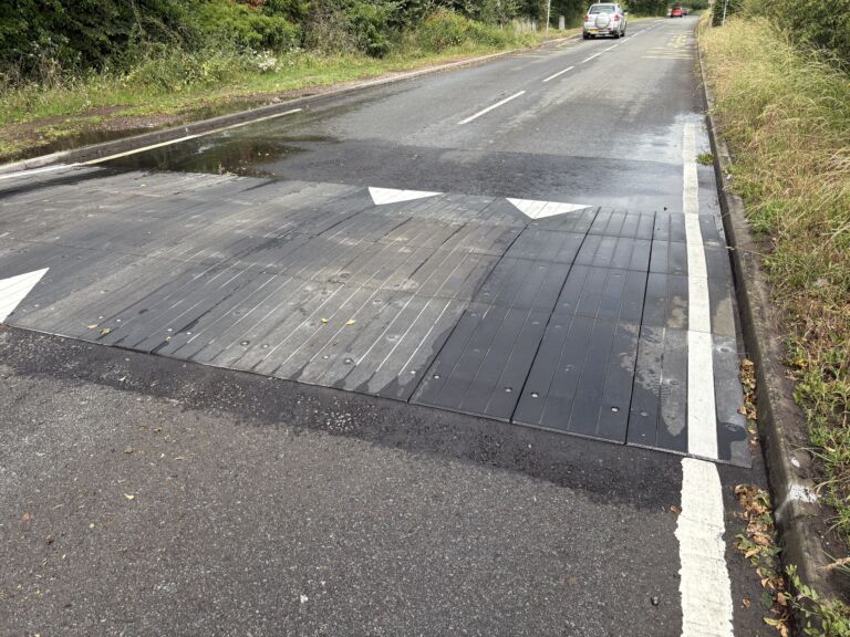 Sinusoidal rubber ramp installed across a full-width roadway, providing smooth traffic calming with directional road markings