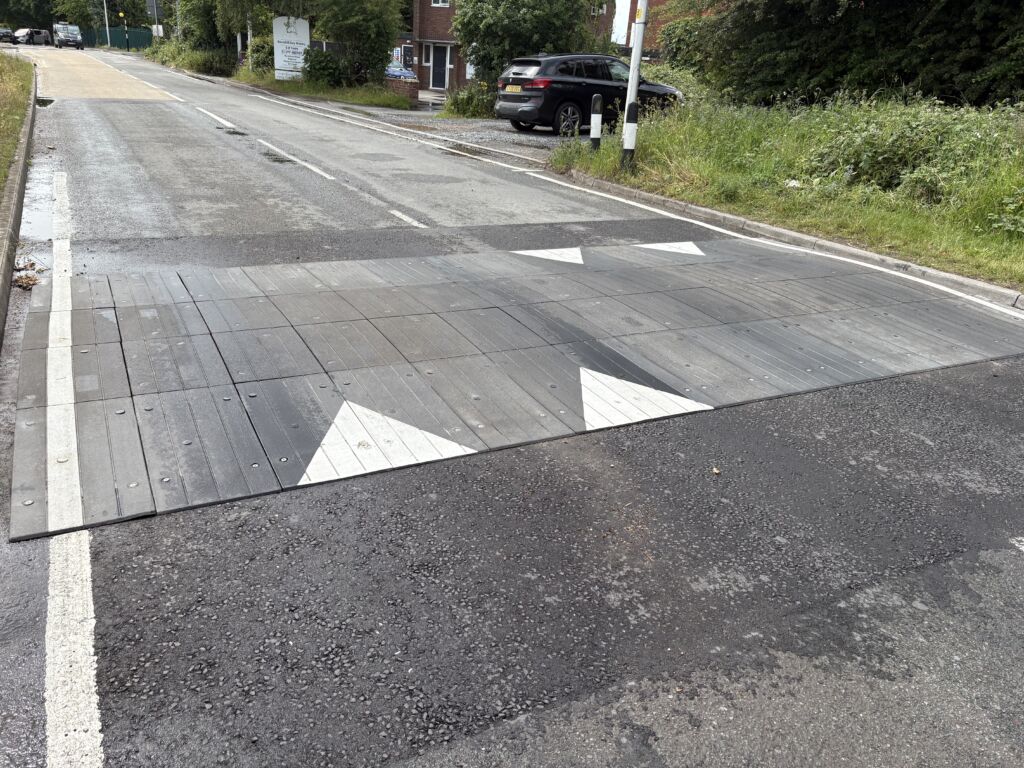 Sinusoidal rubber ramp installed across a full-width roadway, providing smooth traffic calming with directional road markings.