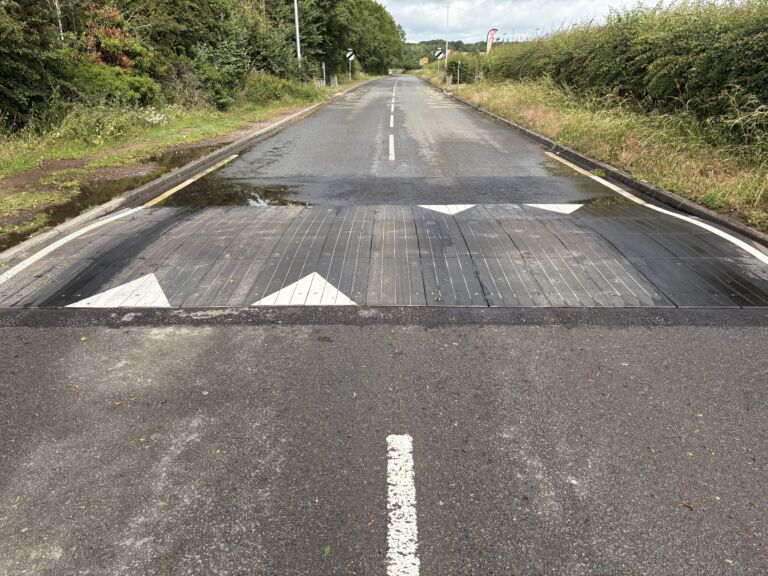 Sinusoidal rubber ramp installed across a full-width roadway, providing smooth traffic calming with directional road markings