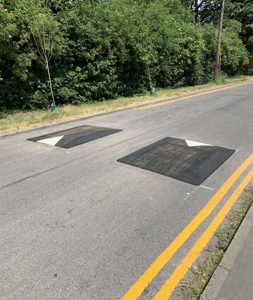 Two black Rediweld Traficop speed cushions installed across a road, positioned in series with white directional arrows on each unit to guide vehicle traffic