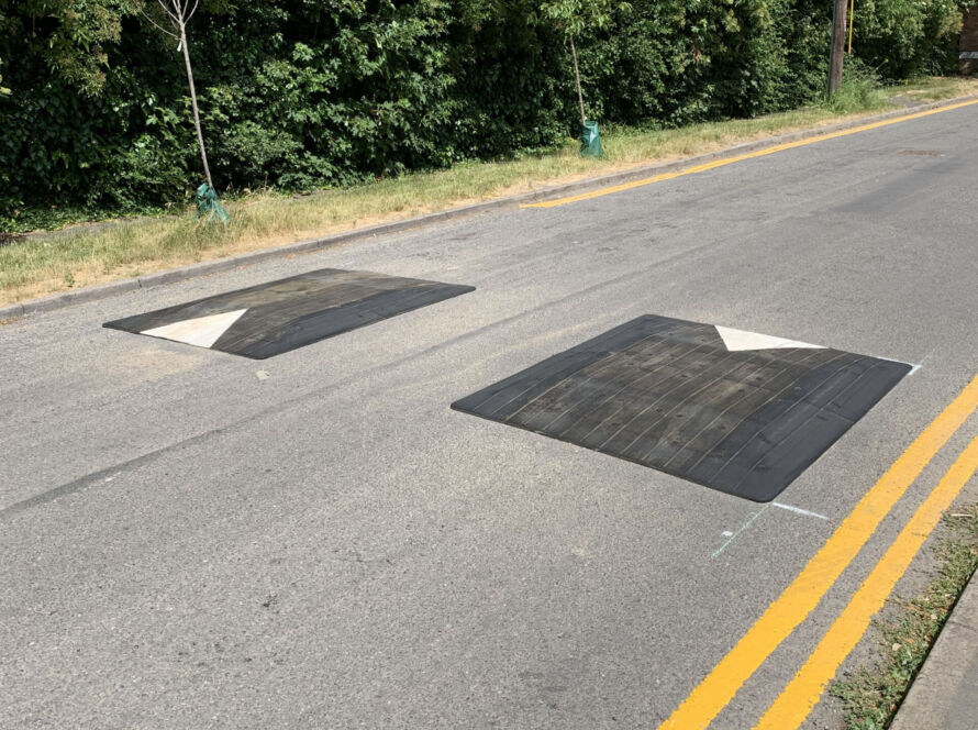 Two black Rediweld Traficop speed cushions installed across a road, positioned in series with white directional arrows on each unit to guide vehicle traffic