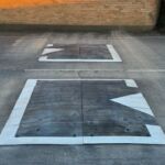 Two Traficop rubber speed cushions installed in series on a roadway, each outlined with white edge markings and directional arrows.