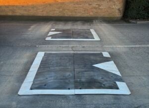 Two Traficop rubber speed cushions installed in series on a roadway, each outlined with white edge markings and directional arrows.
