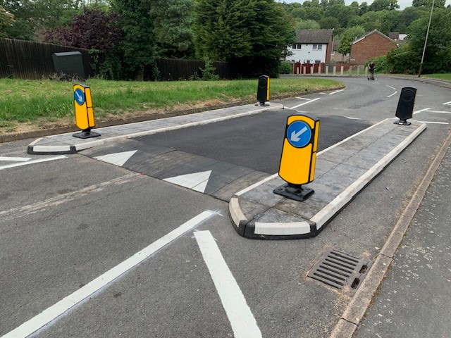 Pedestrian walking alongside newly installed speed table and traffic island system on a residential road.