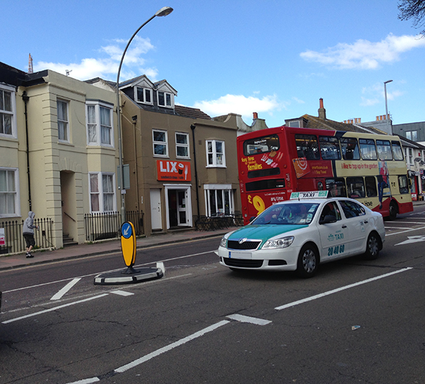 Black and white RediPave traffic island with directional bollard separating lanes on urban street.