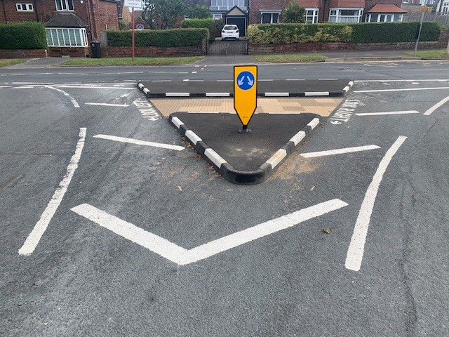 Triangular traffic island with kerbed edging and central directional bollard at residential road junction.