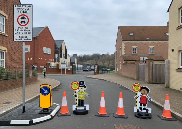 Temporary school street closure with traffic cones, bollard, and child-shaped ‘stop’ signs blocking road outside residential area