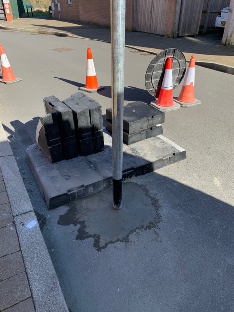 Close-up of installed signpost base with modular blocks and traffic cones during street works