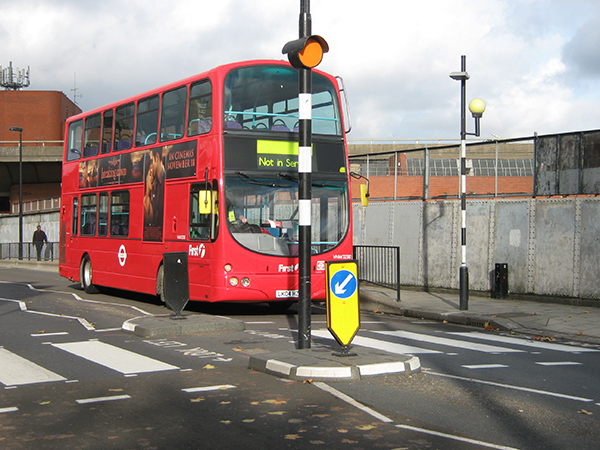 Grey and white RediPave traffic island with directional bollard separating lanes near pedestrian crossing