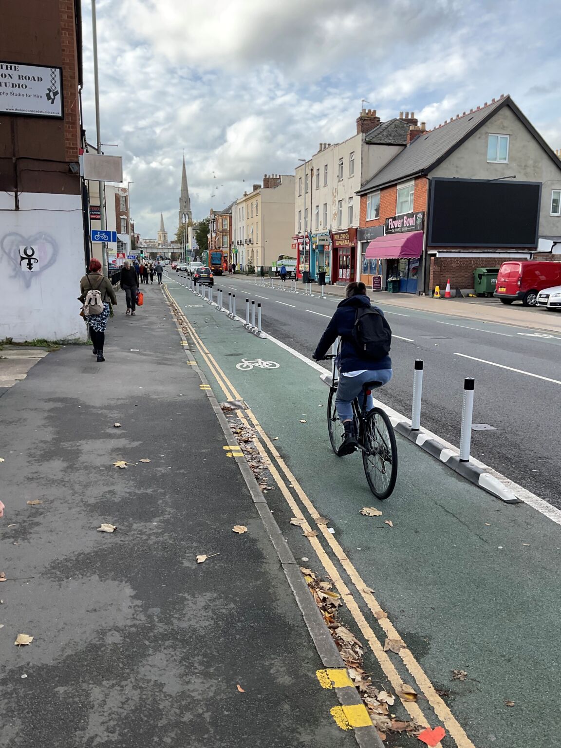 Cyclist riding in a protected bike lane separated from traffic by flexible bollards on a busy urban street